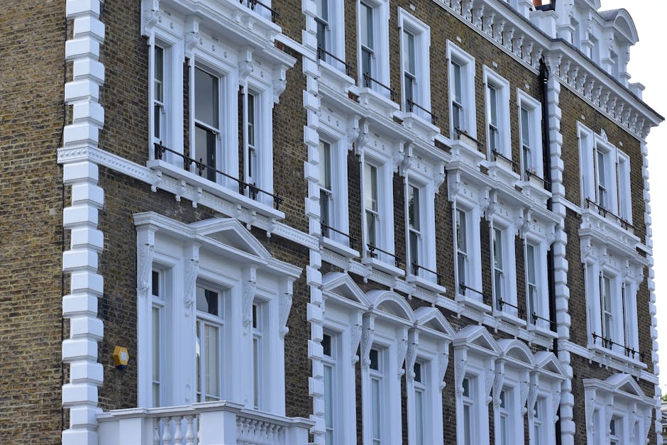 A low-angle view of a Victorian terraced building in Clapham Common, featuring ornate white decorative elements and red brickwork with white accents. The building has tall, narrow windows with white f