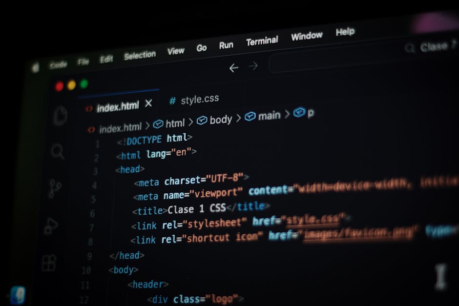 A person wearing a light blue shirt is seated at a desk, working on a laptop with a black screen displaying multicolored lines of code. The individual's right hand is holding a stylus, pointing at the